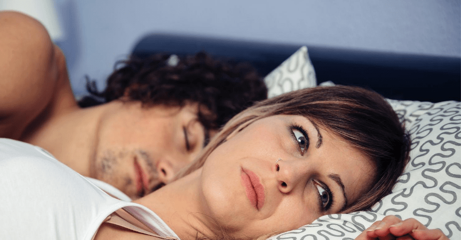 woman-thinking-in-bed-with-husband-sleeping