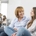 affectionate mother and daughter sitting on sofa with family in background