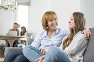 affectionate mother and daughter sitting on sofa with family in background